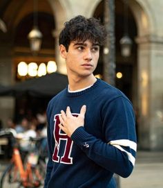 a young man standing in front of a building with his hands clasped to his chest