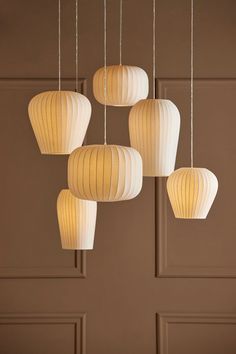 five white lanterns hanging from the ceiling in front of a brown wall with wooden paneling