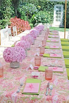 a long table is set with pink and green place settings for an outdoor dinner party