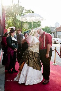 a man and woman dressed in period clothing kissing under an umbrella on the red carpet