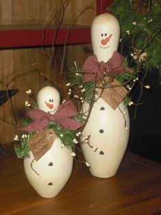 two snowmen sitting next to each other on top of a wooden table in front of a potted plant