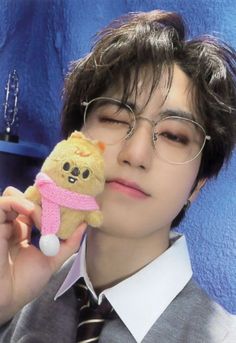 a man holding a teddy bear in his right hand while wearing glasses and a tie