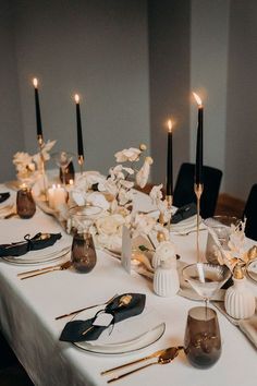 the table is set with black and white plates, silverware, candles and flowers