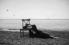 a woman laying on top of a wooden chair next to the ocean