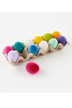 an egg carton filled with different colored eggs and two pom - poms