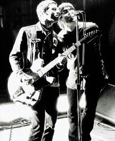 black and white photograph of two people playing guitar on stage with microphone in front of them