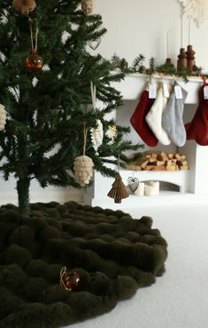 a christmas tree with stockings hanging from it's branches and ornaments on the ground