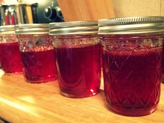 four jars filled with red liquid sitting on top of a wooden counter next to a cutting board