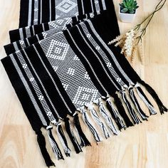 four black and white scarfs sitting on top of a wooden floor next to a potted plant