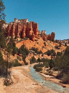 a river running through a lush green forest next to tall red rock formations in the distance