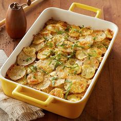 a casserole dish filled with potatoes and garnished with green herbs on a wooden table