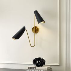 two black and gold wall lights next to each other on a white wall in a room