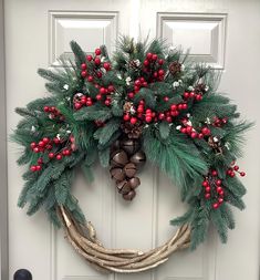 a wreath is hanging on the front door with bells and evergreen leaves, berries, and pine cones