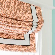 an orange and white roman blind with black trim on the top, in front of a window