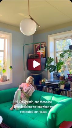 a woman sitting on top of a green couch in a living room next to two windows