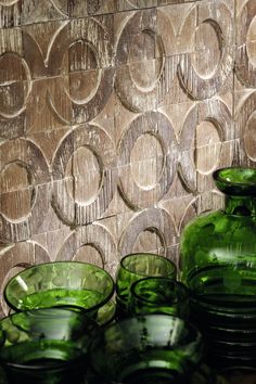 several green glass bowls and vases on a table with a wood wall behind them