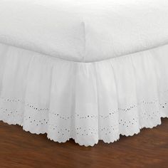 a white bed skirt on top of a wooden floor