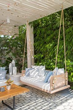 a porch swing with cushions and pillows hanging from it's sides in front of a green wall