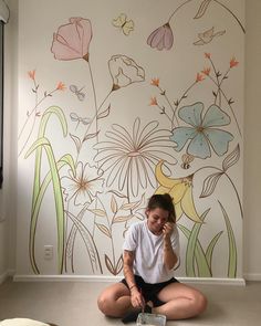 a woman sitting on the floor in front of a wall with flowers painted on it