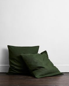 two dark green pillows sitting on top of a wooden floor next to a white wall