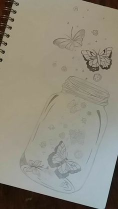 a drawing of a jar with butterflies in it on top of a table next to a notebook