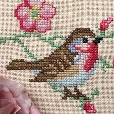 a cross stitch pattern with a bird on a branch and pink flowers in the background