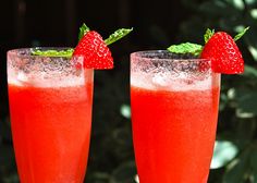 two glasses filled with red liquid and topped with strawberries on the rim, sitting next to each other