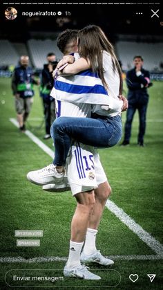 a man and woman hug on the back of each other as they stand on a soccer field