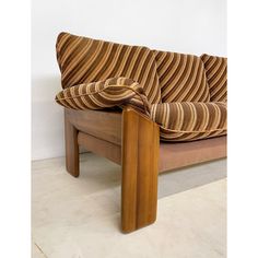 a wooden couch with striped fabric on it's back and arm rests against a white wall