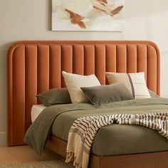 an orange headboard on a bed with pillows and blankets in the foreground is a painting hanging above it