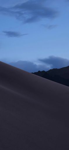 a person riding a surfboard on top of a large sand dune at night with mountains in the background