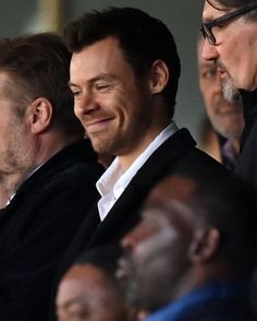 two men sitting next to each other in front of a group of people wearing suits