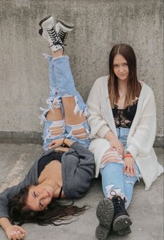 two young women sitting on the ground with their legs crossed and one holding her leg up