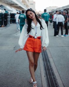 a woman is walking down the street wearing an orange skirt and white shirt with her hands in her pockets