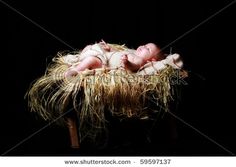 a baby laying on top of a pile of hay next to a wooden chair and black background