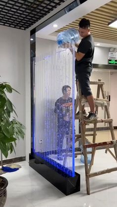 a man standing on a ladder next to a tall glass case with blue lights in it