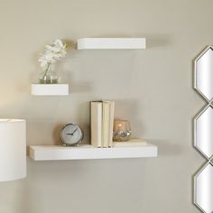 a white shelf with two books and a clock on it next to a wall lamp