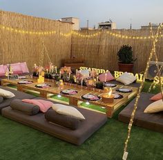 an outdoor seating area with lots of pillows and lights on the grass, in front of a bamboo fence