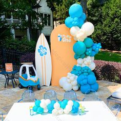 a surfboard and balloon arch is set up on a table outside for a birthday party