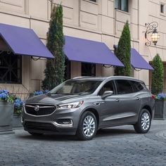 a silver buick suv parked in front of a building with purple awnings and blue flowers