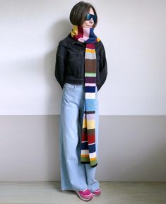 a woman standing in front of a white wall wearing a multicolored striped scarf