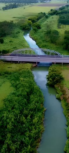 an aerial view of a bridge over a river in the middle of a green field