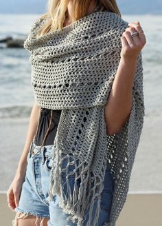 a woman standing on the beach wearing a crocheted shawl over her shoulders