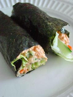 two pieces of sushi on a plate with cucumber, carrots and lettuce