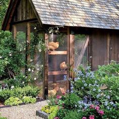 a chicken coop with chickens in it surrounded by flowers and plants on either side of the building