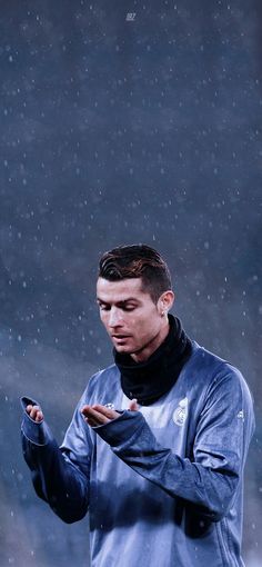 a man standing in the rain holding his hands together and looking at something on his phone