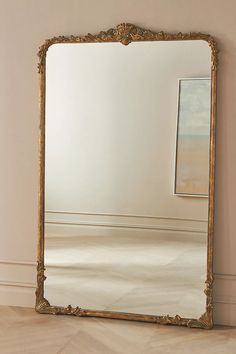 an ornate gold framed mirror on the floor in front of a white wall and beige walls