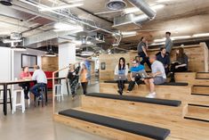 several people are sitting on the stairs in an open space with tables and stools