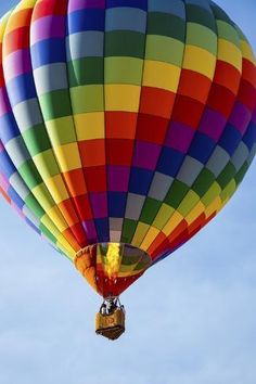 a multicolored hot air balloon flying in the sky with blue skies behind it