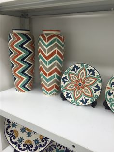 several decorative vases and plates on a shelf in a room with white shelving